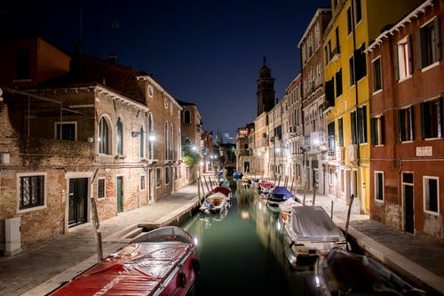 Un canale veneziano di notte, tra barche ormeggiate e palazzi illuminati.